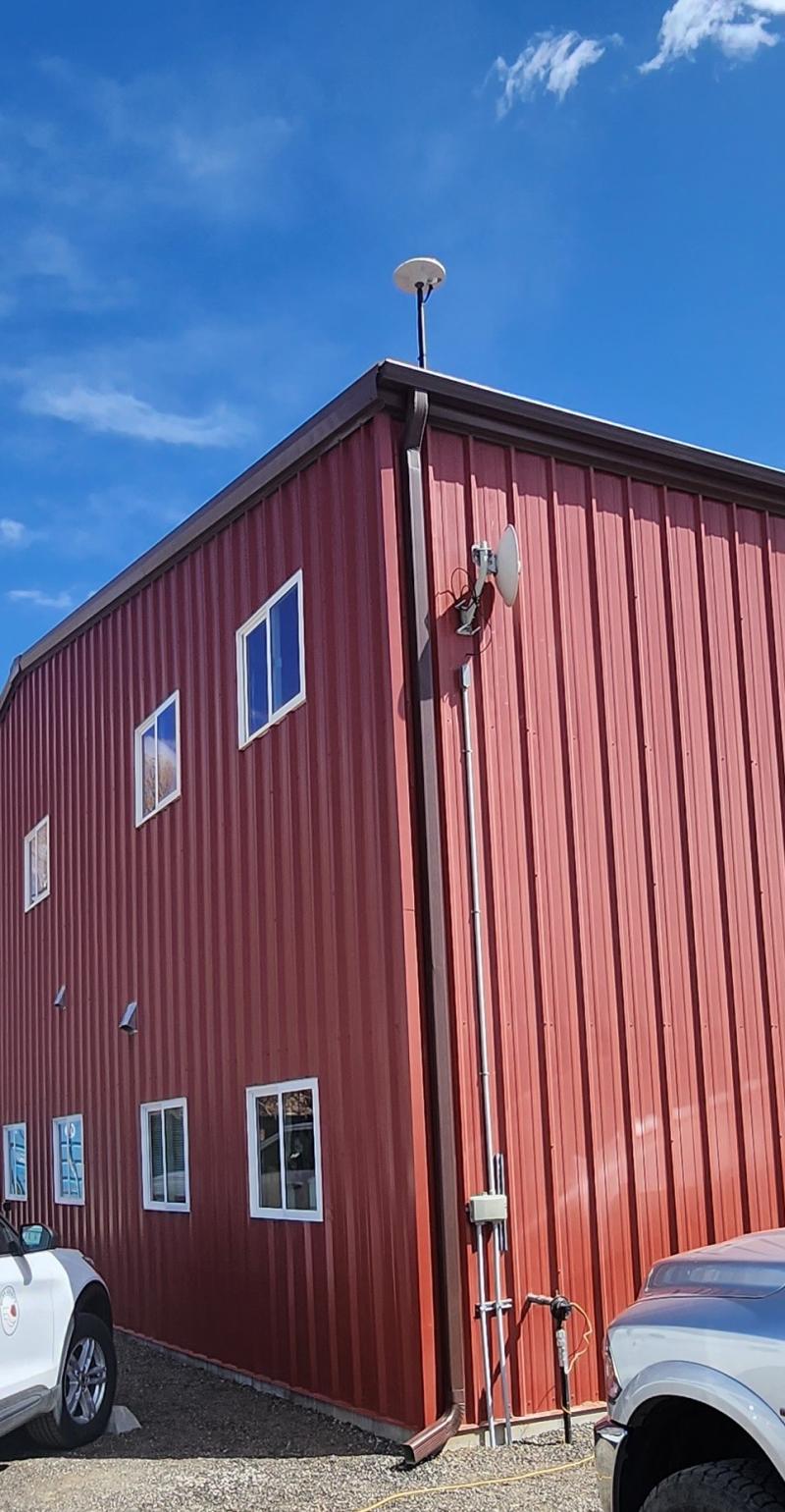 Antenna situated on top of two story, red metal building with a blue sky framing the building.
