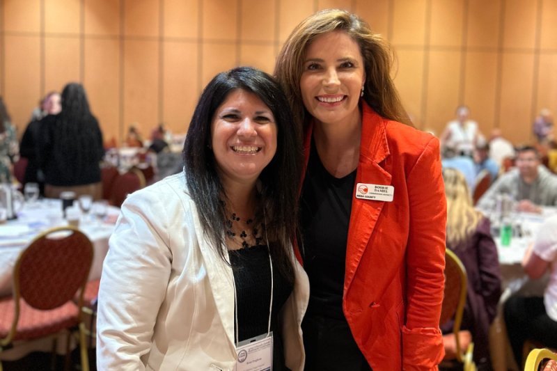 Two women smiling at the 3rd Annual Opioid Abatement Conference, with the woman on the right wearing a name tag identifying her as Bobbie Daniel from Mesa County.