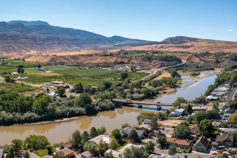 Aerial view of Palisade featuring green vineyards, farmland, and a winding river crossed by a small bridge.