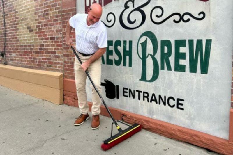 Man sweeping sidewalk with a smile on his face. 