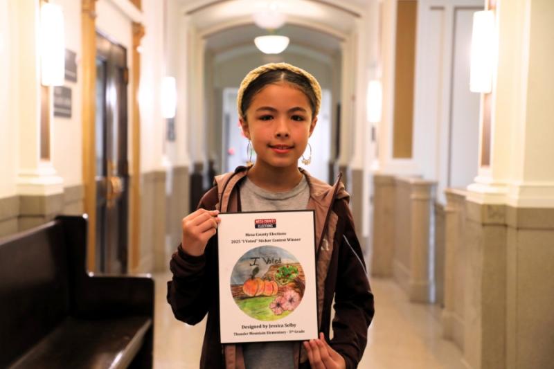 A child smiling holding a framed drawing. 