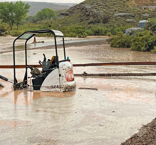 A construction vehicle partially submerged in muddy flood water.