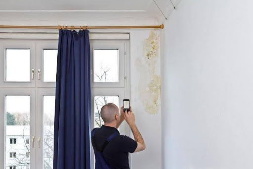 A man using his cell phone to take a picture of flood damage to a wall.
