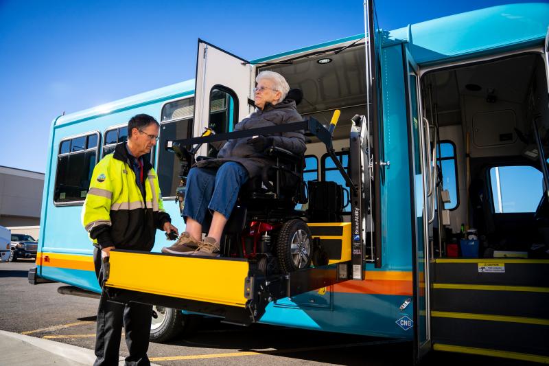 Photo of a Grand Valley Transit employee assisting a wheelchair-bound rider get on the Paratransit vehicle using a lift.