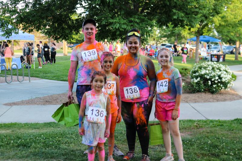 A family stands outside covered in neon colored glow powder smiling before a fundraiser race.