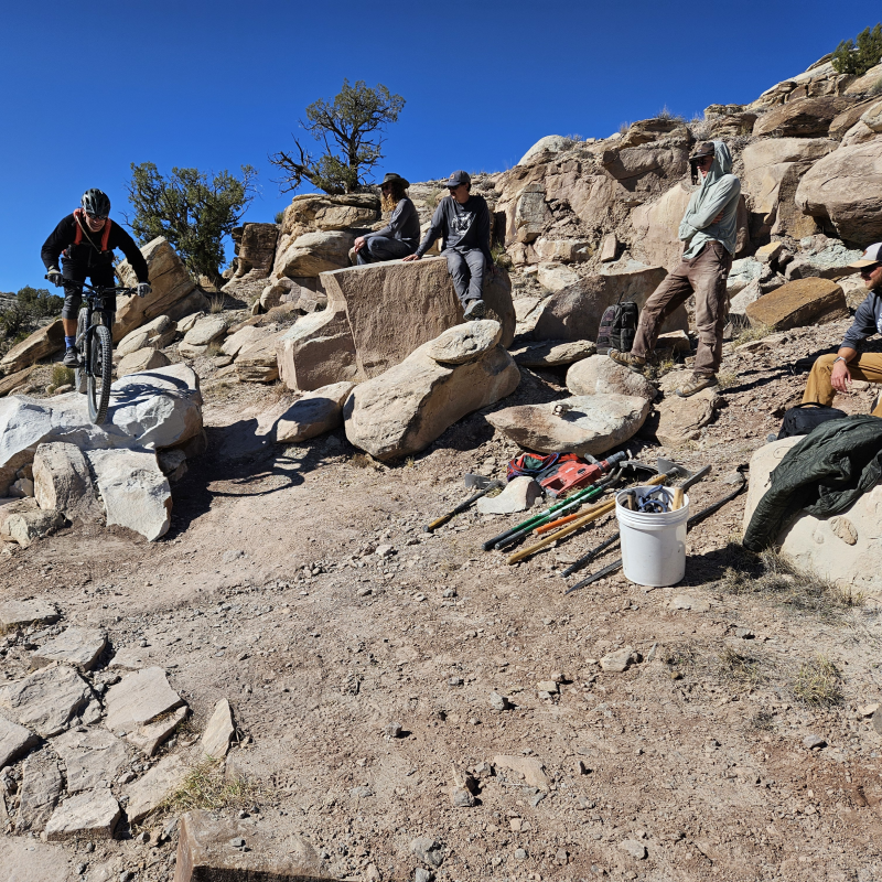 A mountain biker is riding a new rock ramp feature on Wrangler trail at Kokopelli that the trail crew comprised of 4 people finalized construction.