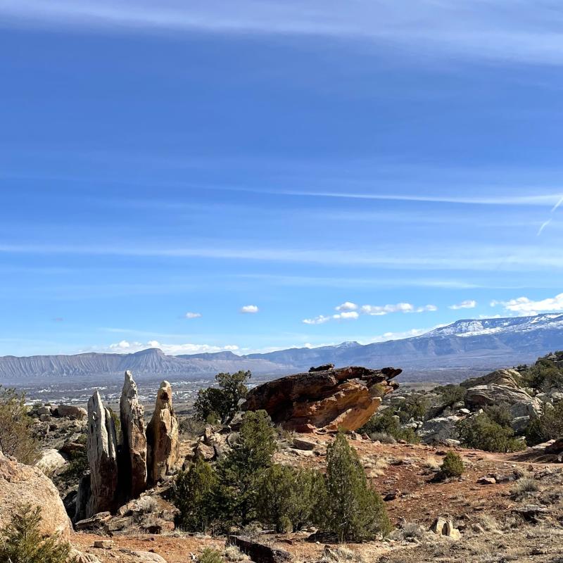 This is called High Noon trail at the Lunch Loops trail system that overlooks the vertical rock slabs, the Book Cliffs, Mount Garfield, and the Grand Mesa covered in springtime snow.