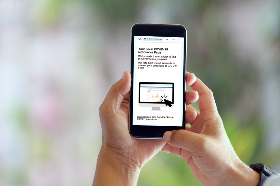 Two hands holding a smartphone that shows an image of the Mesa County Public Health COVID-19 page.