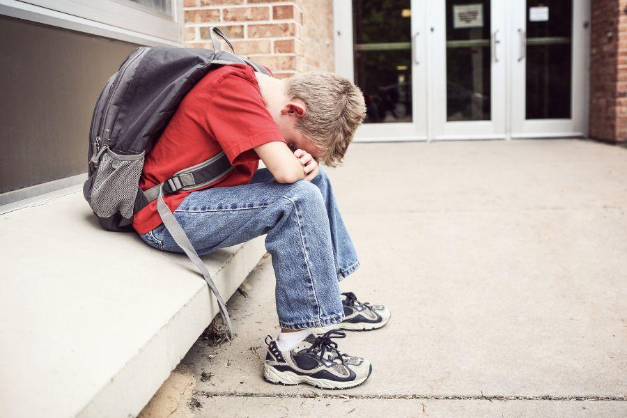 A sad boy sits on steps with his head down
