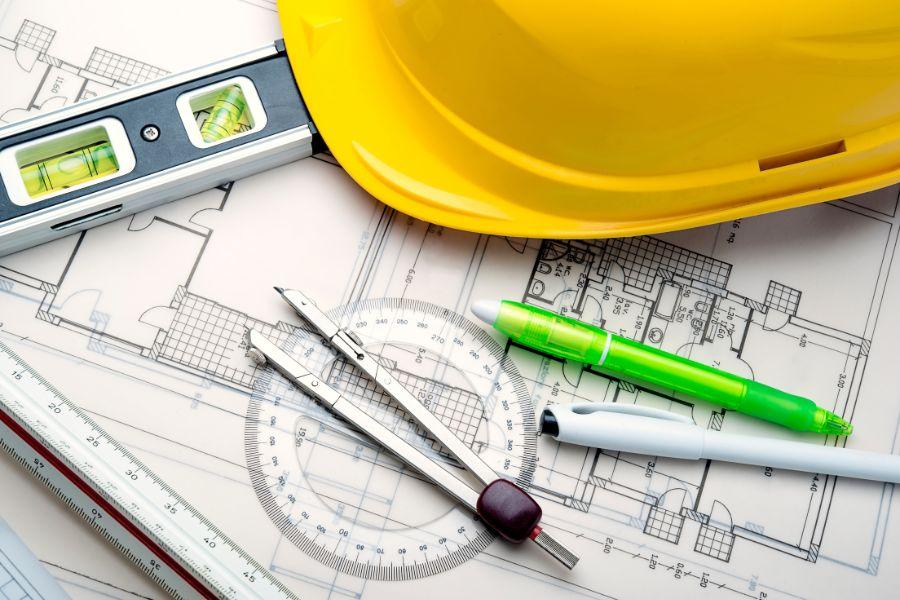 Yellow construction hat and tools sit on engineering plans. 