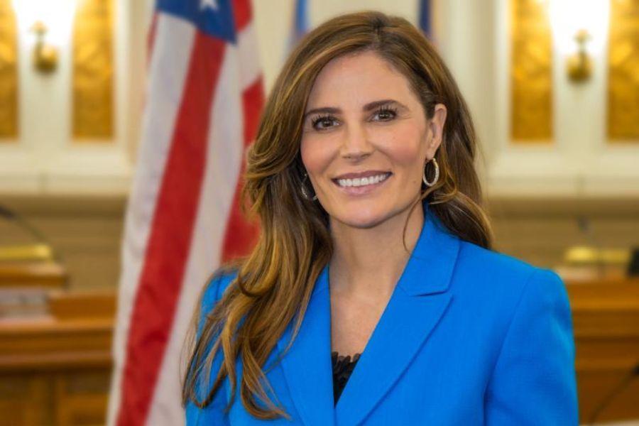 Bobbie Daniel, Chair to the Board of Mesa County Commissioners smiling for a headshot in a blue suit in front of the American flag. 