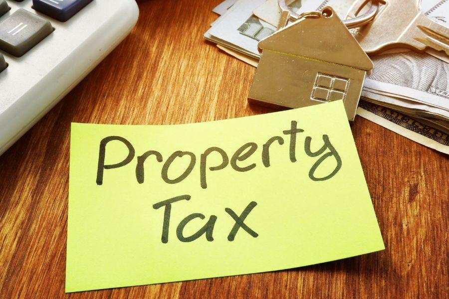 Bright yellow paper reading "Property Tax" sits on dark wood table next to silver house keychain. 