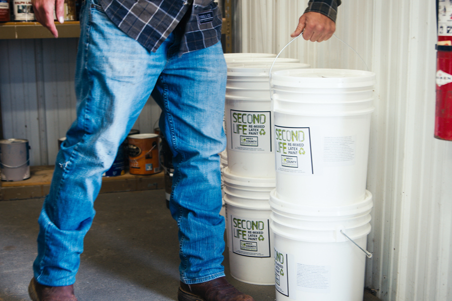 A person holding a five gallon bucket of paint