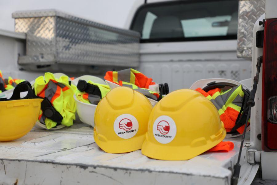 Two yellow Mesa County hard hats on back of white truck. 