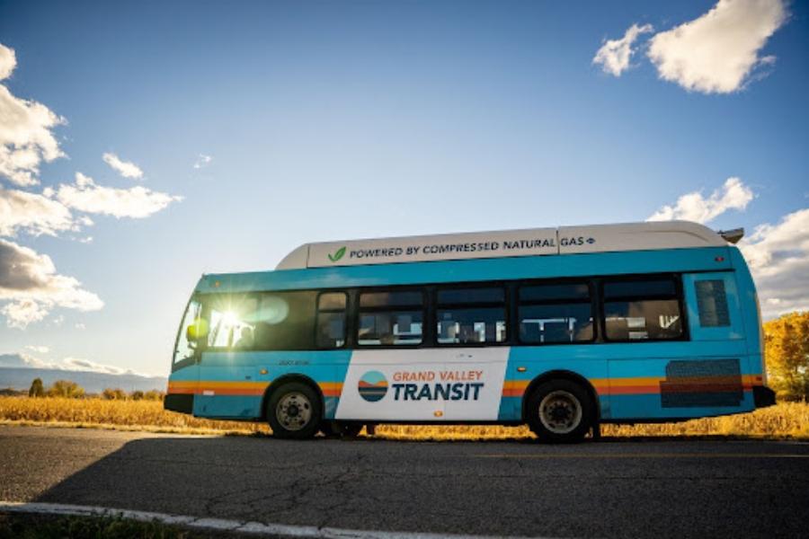 Blue, yellow, orange, and white Grand Valley Transit bus at sunset. 