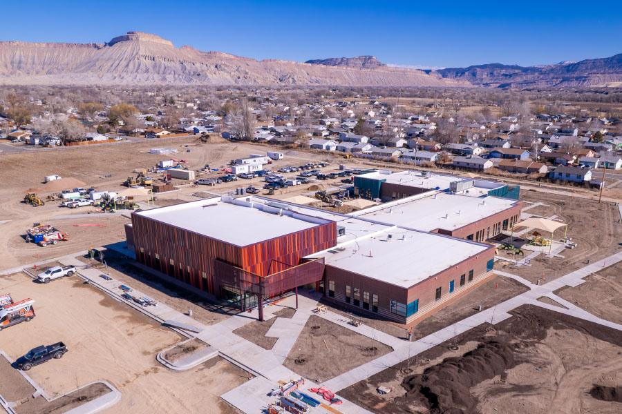 Aerial view of large unfinished red, orange, and brown building with Mt. Garfield in the background. 