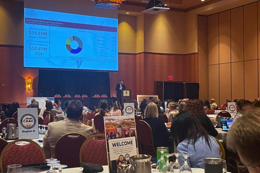 Speaker presenting financial data at the 3rd Annual Opioid Abatement Conference with audience seated at round tables and COAC region signs on tables