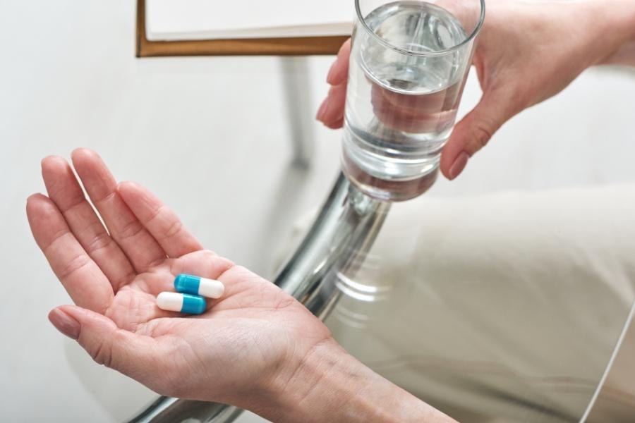 Hands hold two blue and white pills and a glass of water.