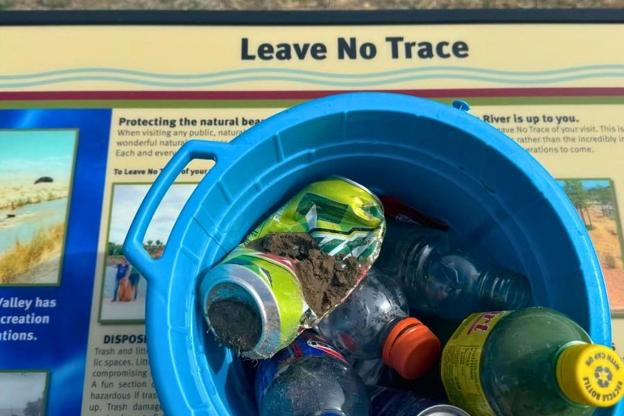 Blue bucket full of trash sitting on yellow sign that reads, "Leave No Trace."