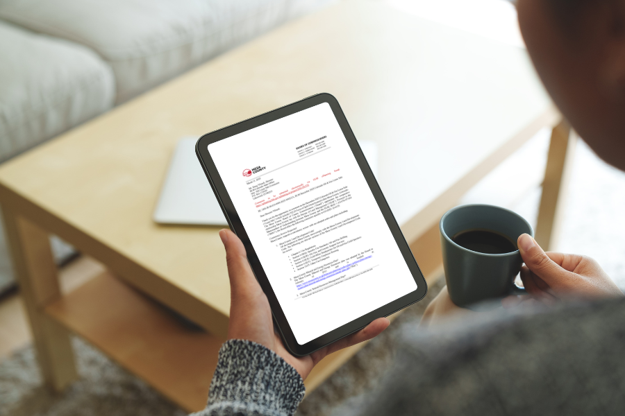 Hands holding an iPad displaying a letter, and a cup of coffee. 