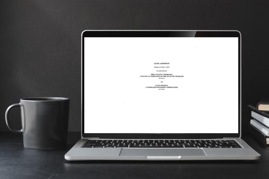 An open laptop on a black desk displaying the first page of a lease agreement next to a grey mug. 