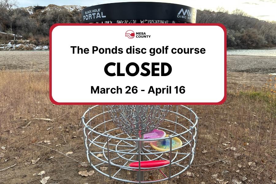 Disc golf basket with three frisbees inside and a white element on top with the Mesa County logo and black text reading, The Ponds disc golf course CLOSED March 26 - April 16. 