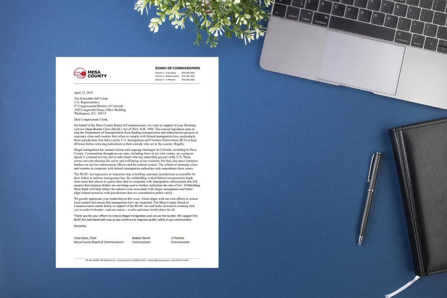 A letter on a blue desk next to a journal, pen, laptop and plant. 