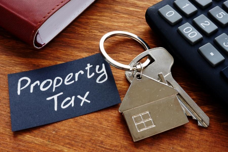 A key with a silver house keychain on it and a black tag reading Property Tax.