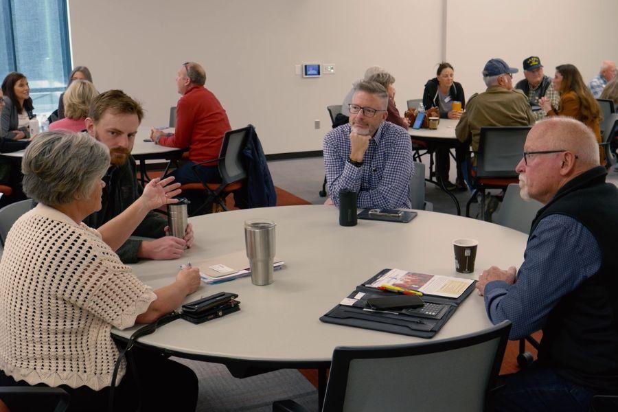 Four individuals sit at a round table engaged in a conversation. 