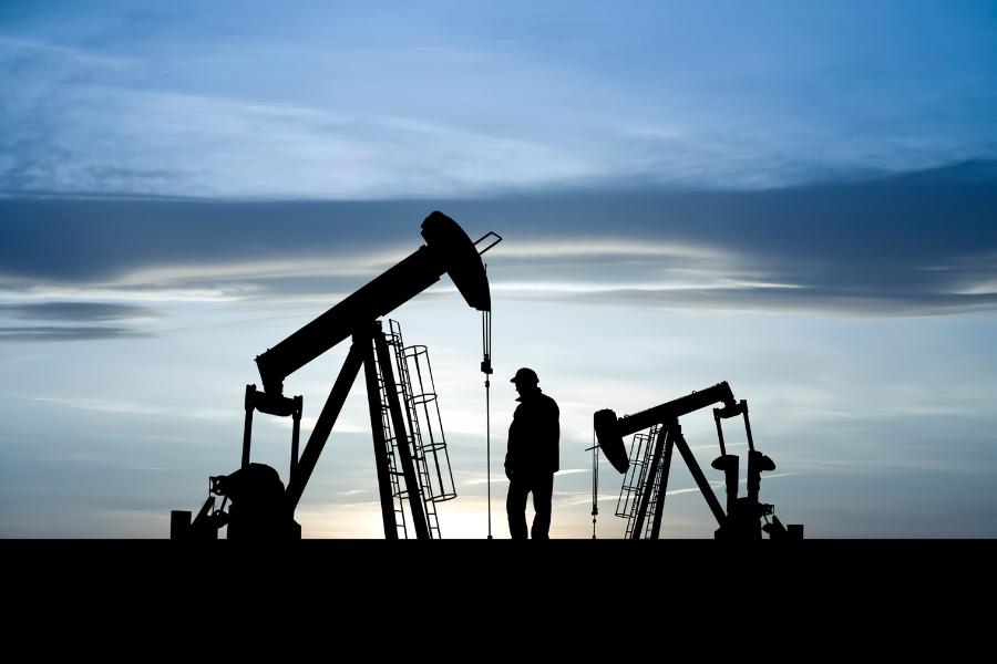 Silhouette of oil and has equipment and a man standing near it at sundown.  