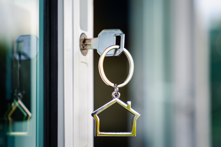 A house key in a door with a silver house keychain on it. 