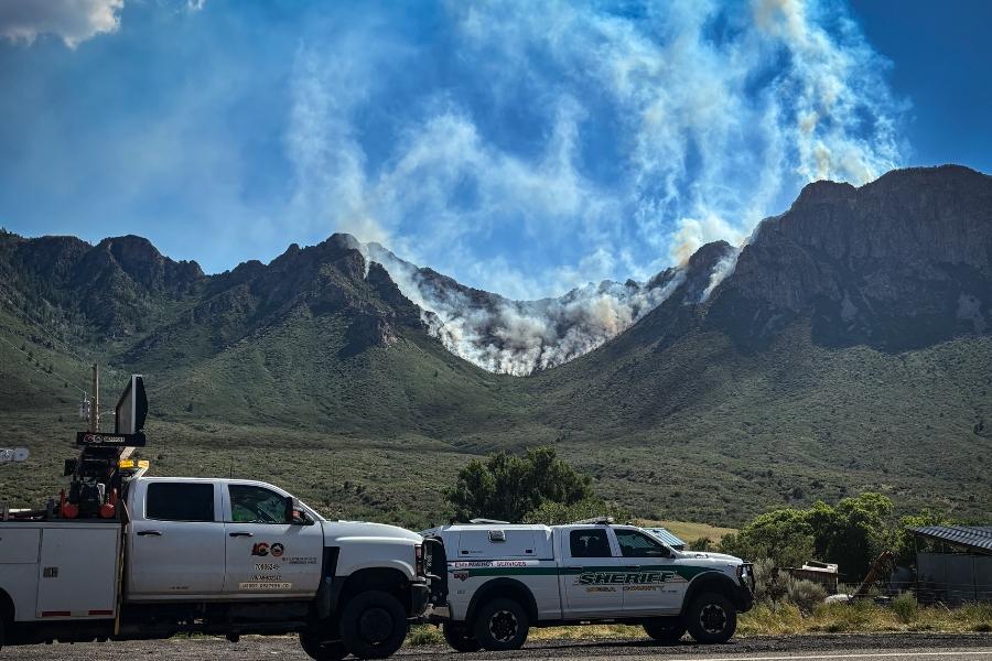 A CDOT truck and a Mesa County Sheriff's Office truck parked near a mountain with wildfire smoke rising. 