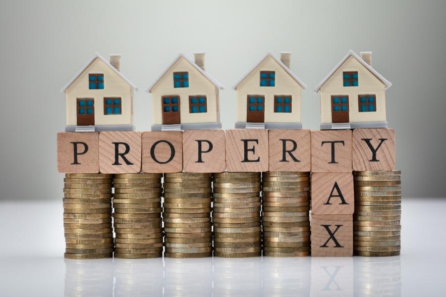 Wooden blocks that read, property taxes, on top of change with toy houses stacked on top. 