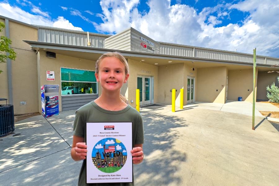 A child holding a plaque in front of the Mesa County Elections building.