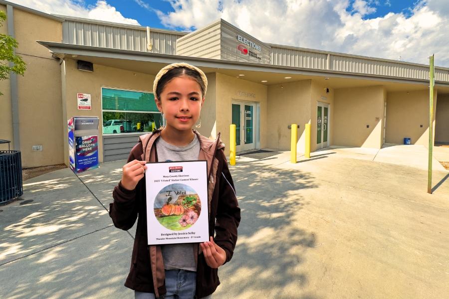 A child holding a plaque in front of the Mesa County Elections building.
