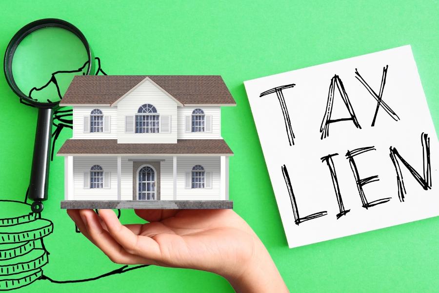 A paper that reads, tax lien, with a hand holding a toy house. 