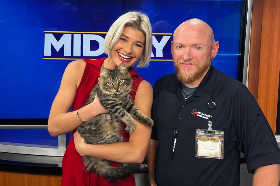 A girl holding a cat, standing next to a man. 