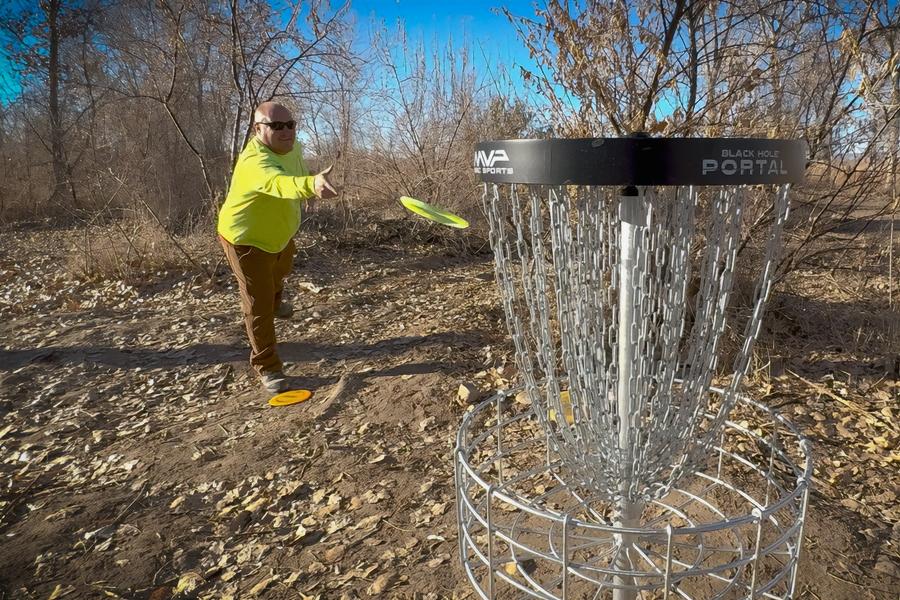 A man throwing a disc into a basket at a disc golf course. 