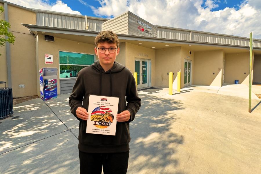 A child holding a plaque in front of the Mesa County Elections building. 