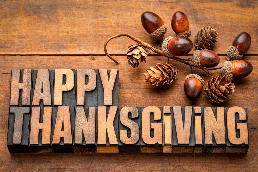 A table with acorns with wooden letters spelling out Happy Thanksgiving. 