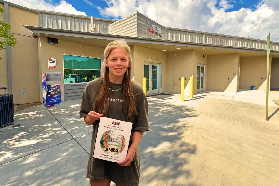 A child holding a plaque in front of the Mesa County Elections office. 