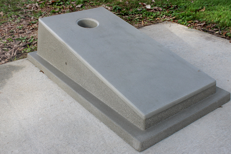 Concrete cornhole board with a circular hole at the top, installed on a concrete pad at Long Family Memorial Park, with grass visible in the background.