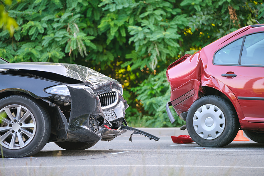 Damaged black and red cars after a rear-end crash on a roadway, with visible front and rear impact damage and debris on the pavement.