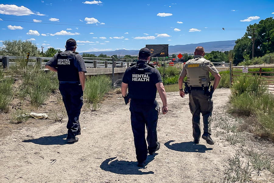 Three Mesa County Sheriff’s Office co-response team members, including behavioral health clinicians and a deputy, walk near a roadway during a community response operation.
