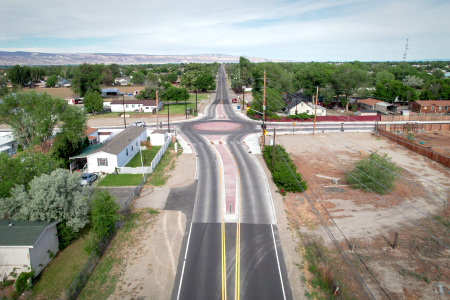 An aerial view of a newly improved roadway and roundabout intersection in a residential area, with homes, trees and mesas visible in the background.