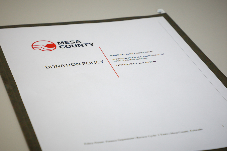 A folder on a desk with a sheet of paper on top that reads “donation policy” and has the Mesa County logo on it. 