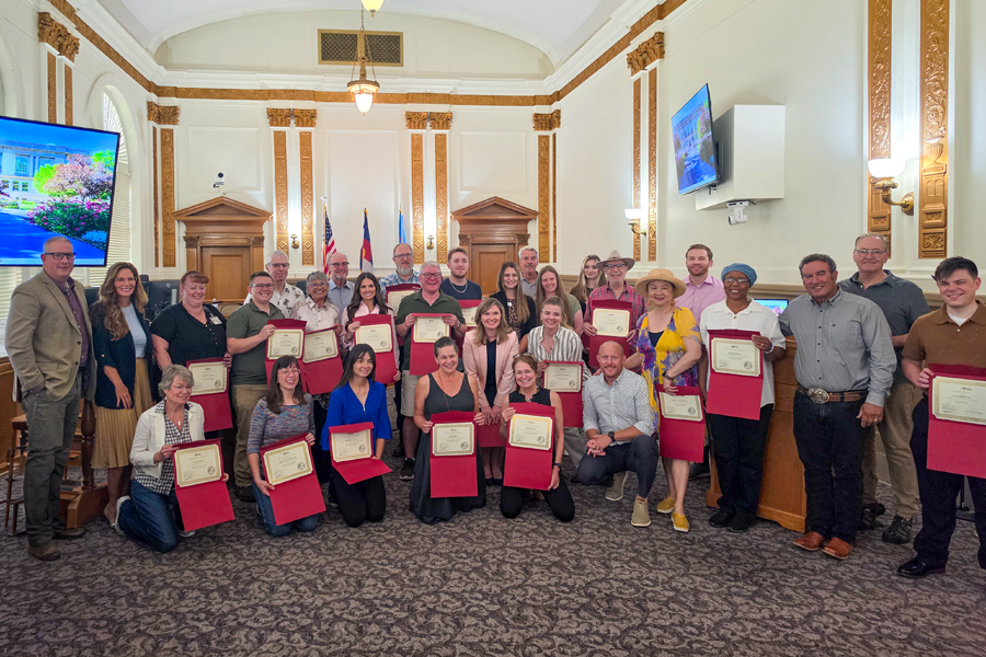 Group photo of about 30 people in the hearing room at the Old Mesa County Courthouse. Most of the people are holding certificates stating they graduated from the Inside Mesa County class.